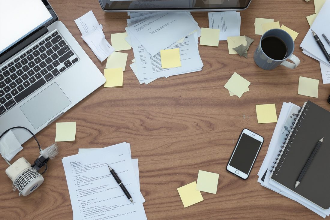 Bureau en désordre couvert de post-it, de papiers épars, d'un ordinateur portable et d'un téléphone
